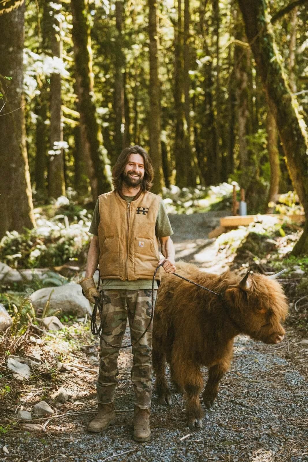Connor smiling on a forest path, leading a Highland calf on a rope