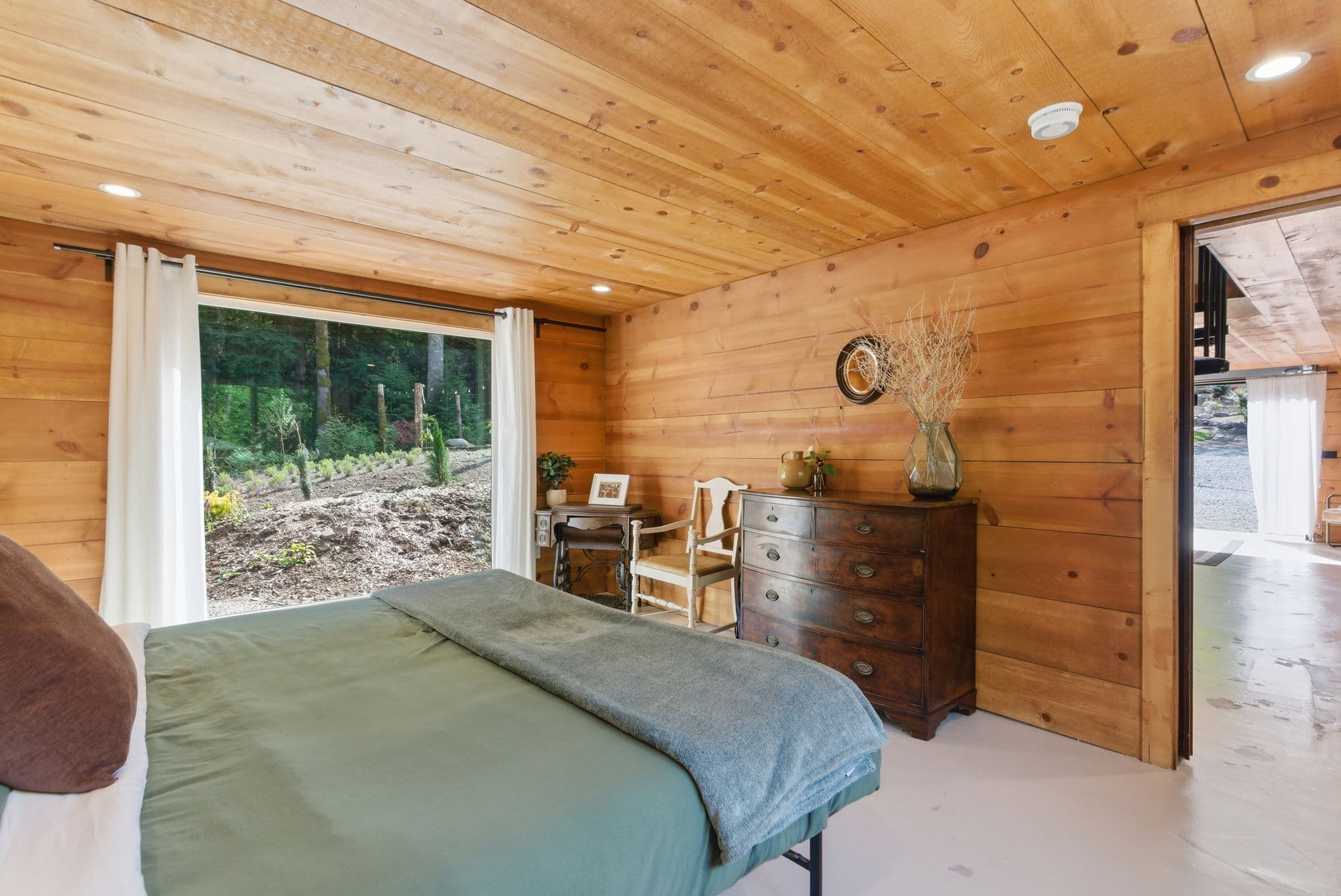 Cedar-walled bedroom with antique dresser and sliding-door forest view