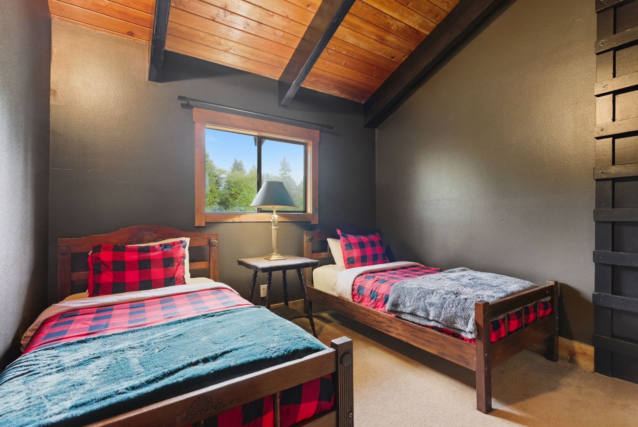 Twin bedroom with lumberjack plaid bedding under a vaulted wood ceiling