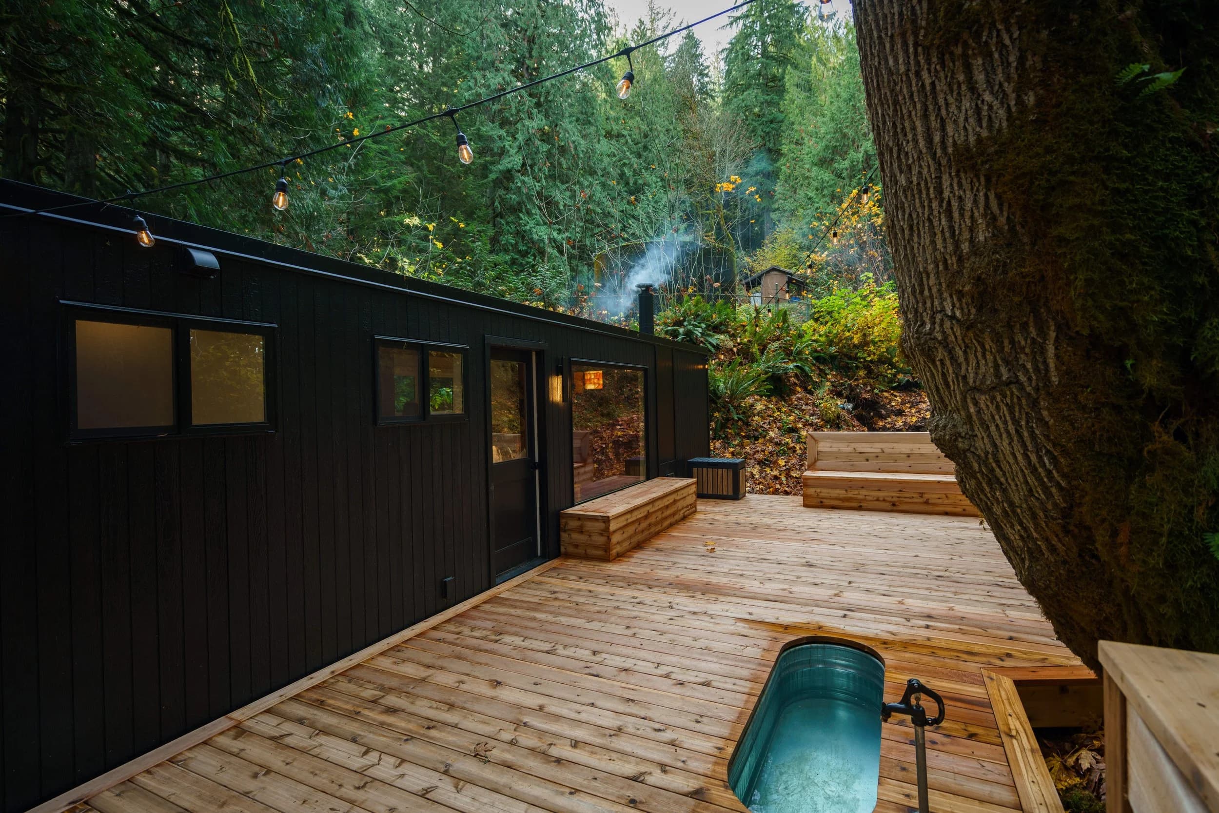 Cedar spa deck at dusk with string lights and the cold plunge tub