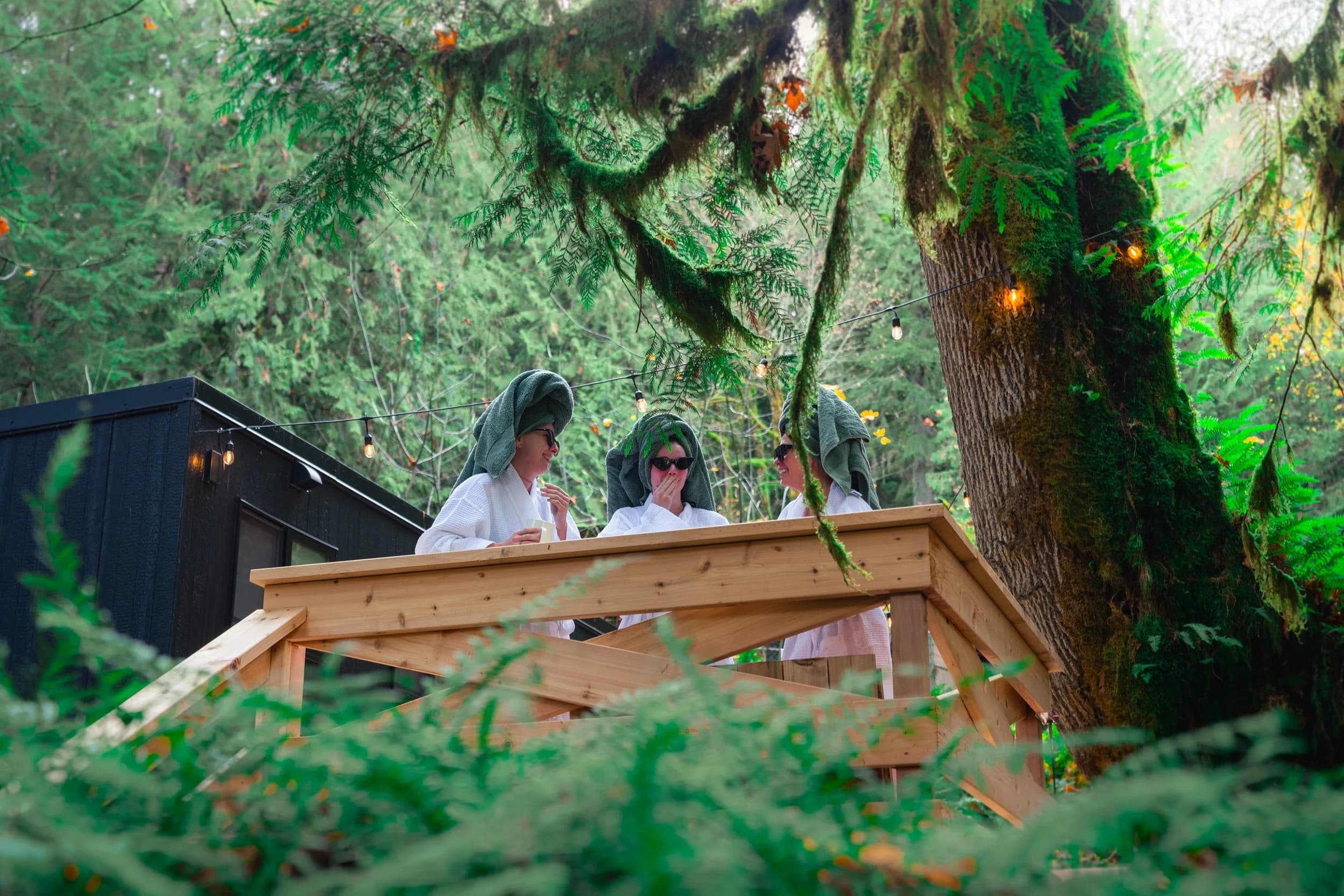 Three guests in white robes leaning on the deck rail among ferns