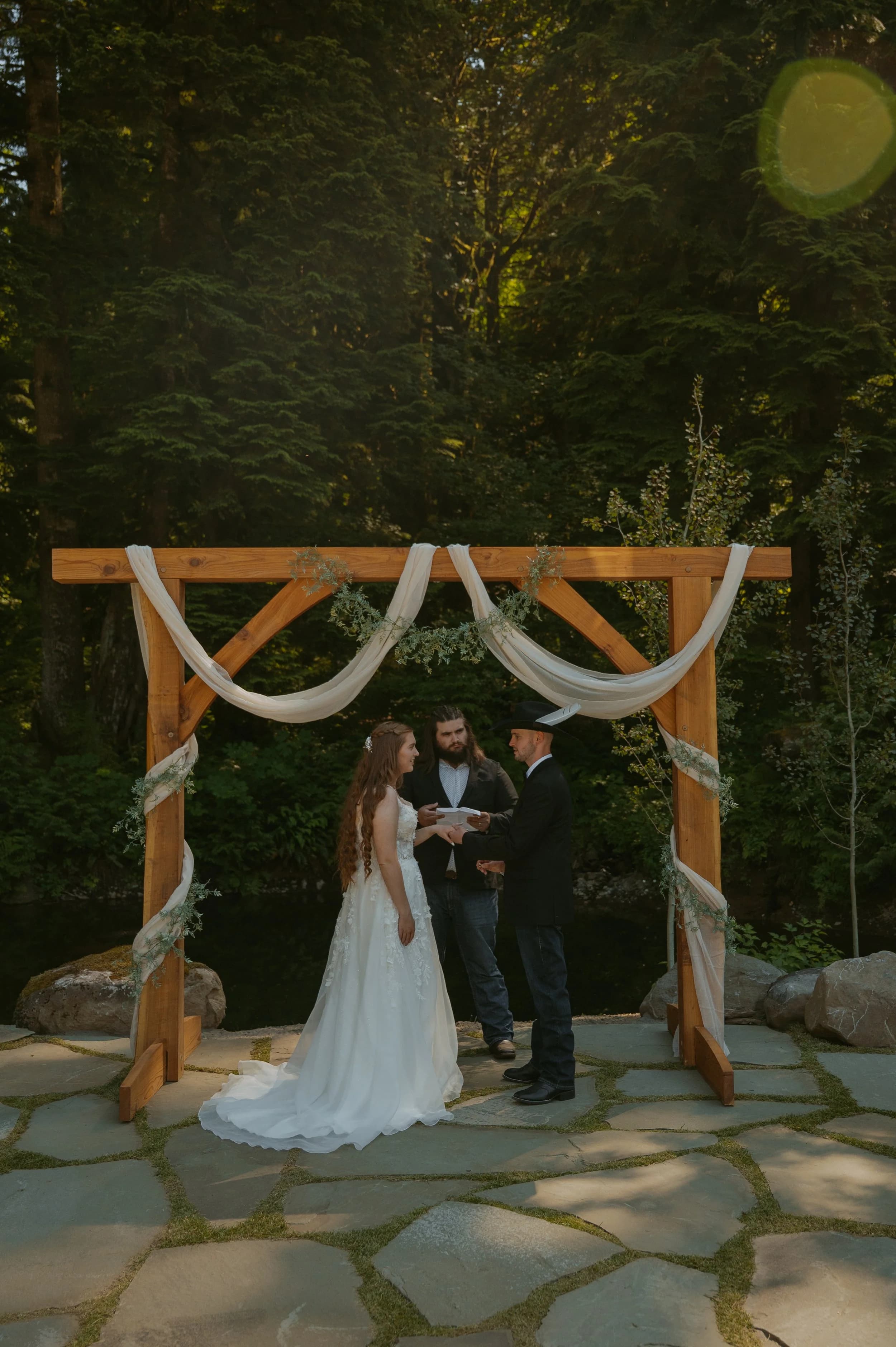 A bride and groom exchange vows under the timber arch in the forest